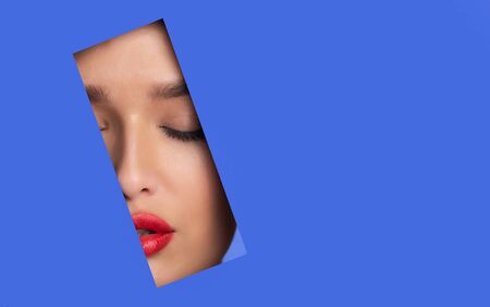 Fashion And Beauty Concept. Attractive girl with red lips peeping out of torn blue paper, empty spaceの写真素材
