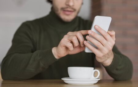 Cropped of guy using modern smartphone and cup of cofee, cafe interior
