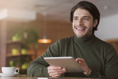 Excited young man using digital tablet while having coffee break at cafe, looking at copy spaceの写真素材