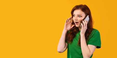 Shocking News. Shocked Teenager Girl Talking On Mobile Phone Standing On Yellow Studio Background. Panorama, Empty Spaceの写真素材
