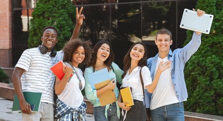 College People. Portrait of happy students with workbooks and laptop posing over campus background, panoramaの写真素材