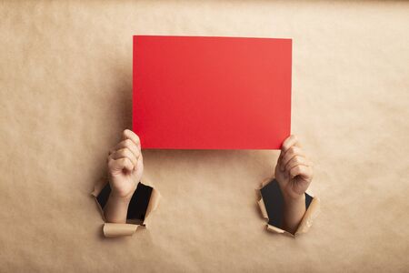 Young girl showing empty red sheet through hole in brown paper, blank space for designの写真素材