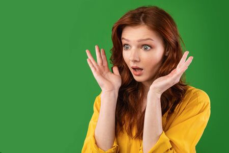 Surprised Girl Looking Aside Holding Hands Near Face Posing On Green Background In Studio. Empty Spaceの写真素材
