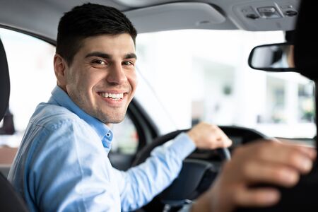 Happy Driver. Handsome man looking back at camera sitting in a car, parking auto, view from rear...