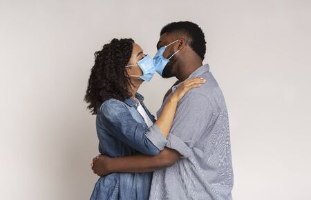 Romantic Black Couple Kissing Each Other In Protective Medical Masks On Face For Corona Virus Spread Prevention, Light Backgroundの写真素材