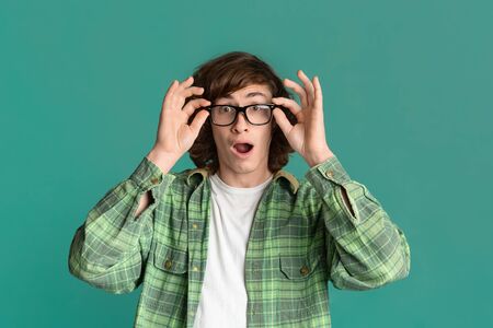Curly young guy with glasses and open mouth feeling shocked on turquoise background
