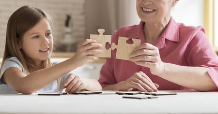 Playing together. Mature lady and her grandchild with puzzle game at table indoors, panoramaの写真素材