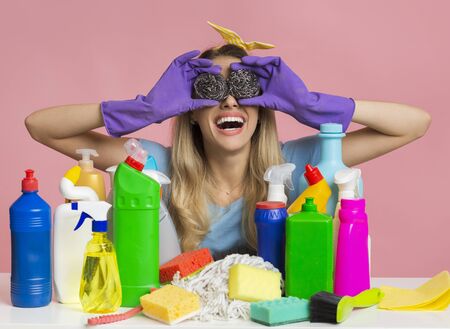 Funny housewife makes glasses with brushes, near cleaning supplies, free space