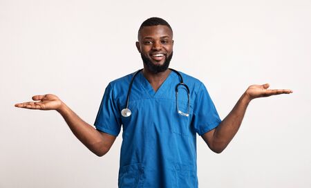 Happy black man therapist in blue uniform with palms up over white studio backgroundの写真素材