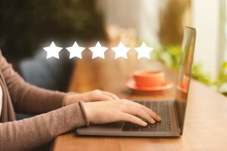 Businesswoman pressing button on high quality rating on laptop, wooden table, blurred background