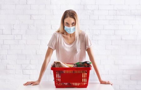 Quarantine at epidemic of COVID-19 virus. Girl in protective mask with basket of productsの写真素材