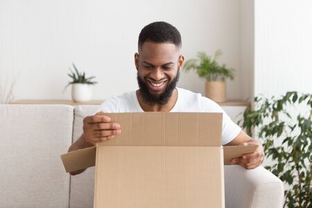 Online shopping at home. Smiling african american guy unpack delivery box