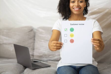 Smiling african american female leaves excellent customer review sitting on sofa, croppedの写真素材