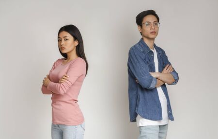 Break up. Upset asian man and woman standing back to back, gray studio background