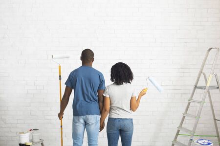 African american guy and girl with rollers in hands paint white brick wall free space, backの写真素材