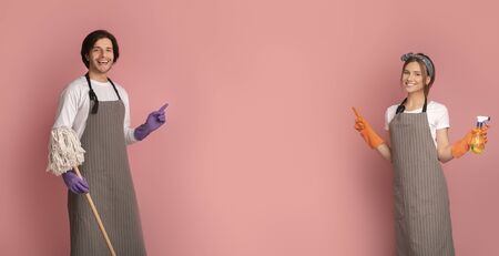 Cheerful Man And Woman With Cleaning Tools In Hands Pointing At Copy Space In The Middle On Pink Background, Panoramaの写真素材