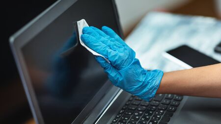 Coronavirus outbreak contamination prevention concept. Female hand in blue gloves cleaning laptop screen with disinfectant clothの写真素材