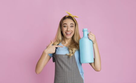 Smiling housewife points finger at fabric softener, on pink background, empty spaceの写真素材