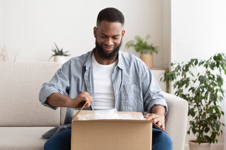 Shopaholic on the couch. African american guy unpacks purchase