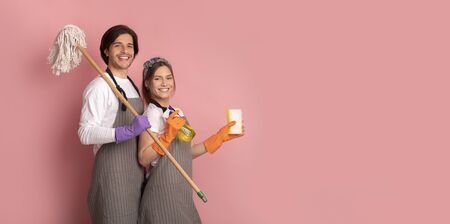 Janitors Team. Happy Man And Woman In Aprons With Cleaning Supplies In Hands Posing Over Pink Background, Panorama With Copy Spaceの写真素材