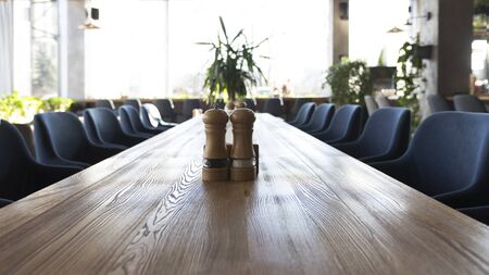 Long wooden table with salt and pepper, interior of modern restaurant, copy spaceの写真素材