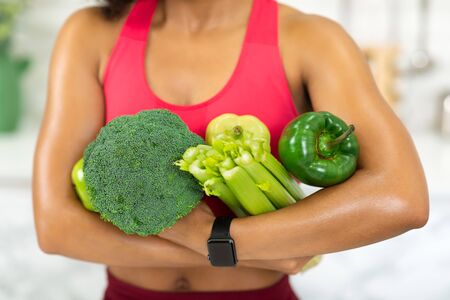 Green Diet Concept. Unrecognizable african woman holding green vegetables in the modern kitchen, selective focusの写真素材