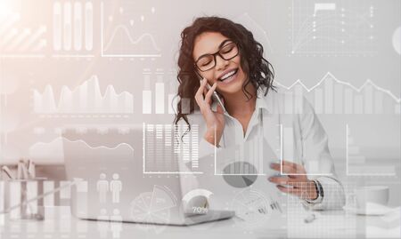 Business technologies concept. Young woman making call while working on laptop in office, collage with graphs on virtual screen. Copy spaceの写真素材