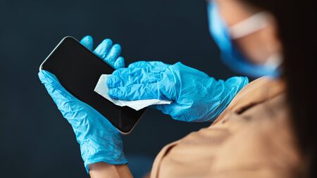 Coronavirus outbreak contamination prevention concept. Woman wearing gloves cleaning mobile phone with disinfectant. Copy spaceの写真素材
