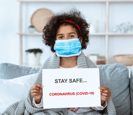 Stay safe during epidemic. Little African American girl holding poster with anti-coronavirus text at homeの写真素材
