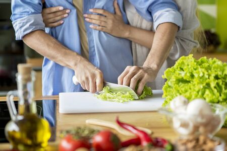 Unrecognizable husband cooking fresh vitamin salad while wife embracing him, happy togetherの写真素材