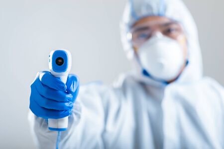 Asian doctor in insulation suit directs infrared thermometer on camera