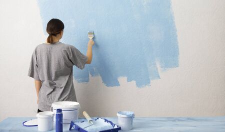 Apartment repair. Woman painting interior wall with paint roller in new houseの写真素材