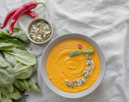 Roasted pumpkin and carrot soup with cream and pumpkin seeds on white table background. Copy space