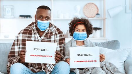 COVID-19 quarantine measures. Little African American girl with her granddad staying at home wearing protective masksの写真素材