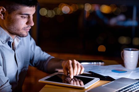 Business Gadgets. Serious Entrepreneur Using Digital Tablet Sitting In Modern Office Working At Night.の写真素材