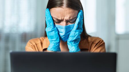 Close up portrait of young woman wearing face mask and gloves covering ears, crying about bad newsの写真素材