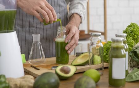 Healthy man enjoys making green vegetables detox cleanse and green fruit smoothie in kitchen at...