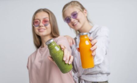 Healthcare and beauty concept. Two girls holding detox smoothie of fresh ingredients on gray backgroundの写真素材