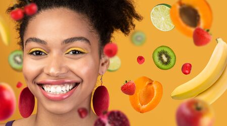 Smiling African American girl on bright summer background with flying fruits, collage. Copy space. Panoramaの写真素材