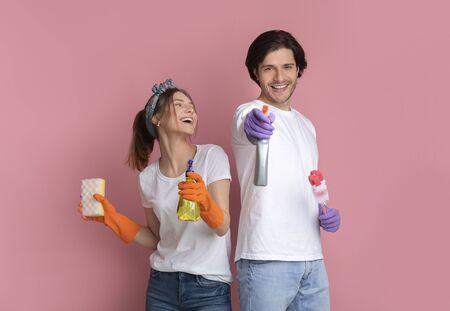 On Guard Of Cleanliness. Joyful millennial couple posing with cleaning supplies on pink background,...