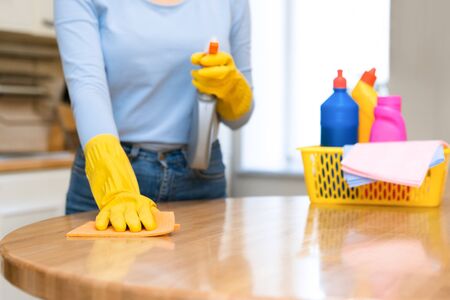 Housemaid Concept. Unrecognizable woman wiping kitchen table with spray and rag, bucket of detergents in backgroundの写真素材