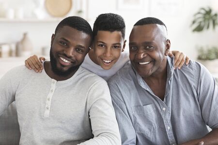 Portrait of happy black son, father and grandfather posing for family picture together, sitting on couch at home and looking at camera, closeupの写真素材