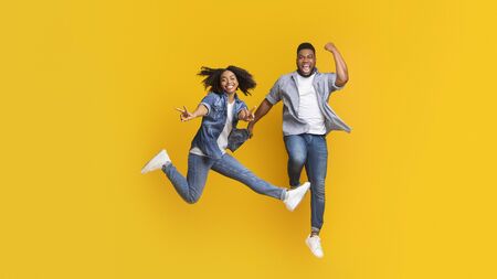 Cheerful African Couple Fooling Together, Jumping In Air And Showing Peace Sign On Yellow Background, Copy Spaceの写真素材
