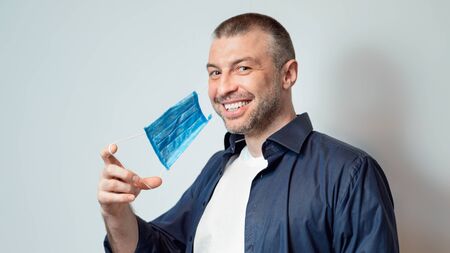 End Of Coronavirus Pandemic. Happy Man Taking Off Medical Mask Smiling To Camera Posing Over Gray Background. Panoramaの写真素材