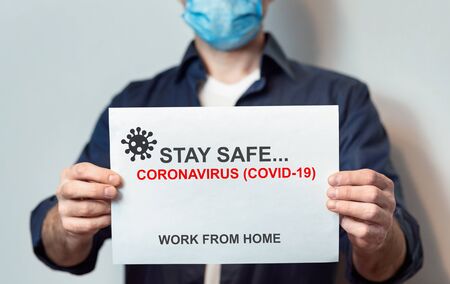 Coronavirus Quarantine. Man In Mask Holding Paper With Inscription Stay Safe, Work From Home Standing Over Gray Background. Croppedの写真素材
