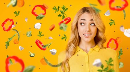 Healthy eating habits. Charming blonde lady on orange background, collage with vegetables flying in air. Panorama with copy spaceの写真素材