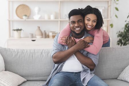 Happy african american couple embracing at home and smiling to camera, enjoying spending quarantine...