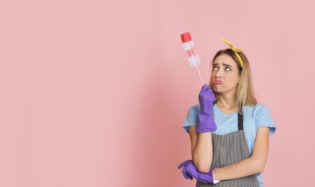 Upset housewife in apron and with rubber gloves looks at brushの写真素材
