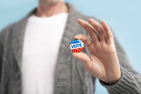 Vote 2020 in America, US. Law abiding american citizen holding vote pin in hand, blurred backgroundの写真素材