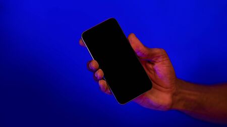 Unrecognizable Man Holding Smartphone With Empty Screen In Hand Advertising Mobile App Over Blue...
